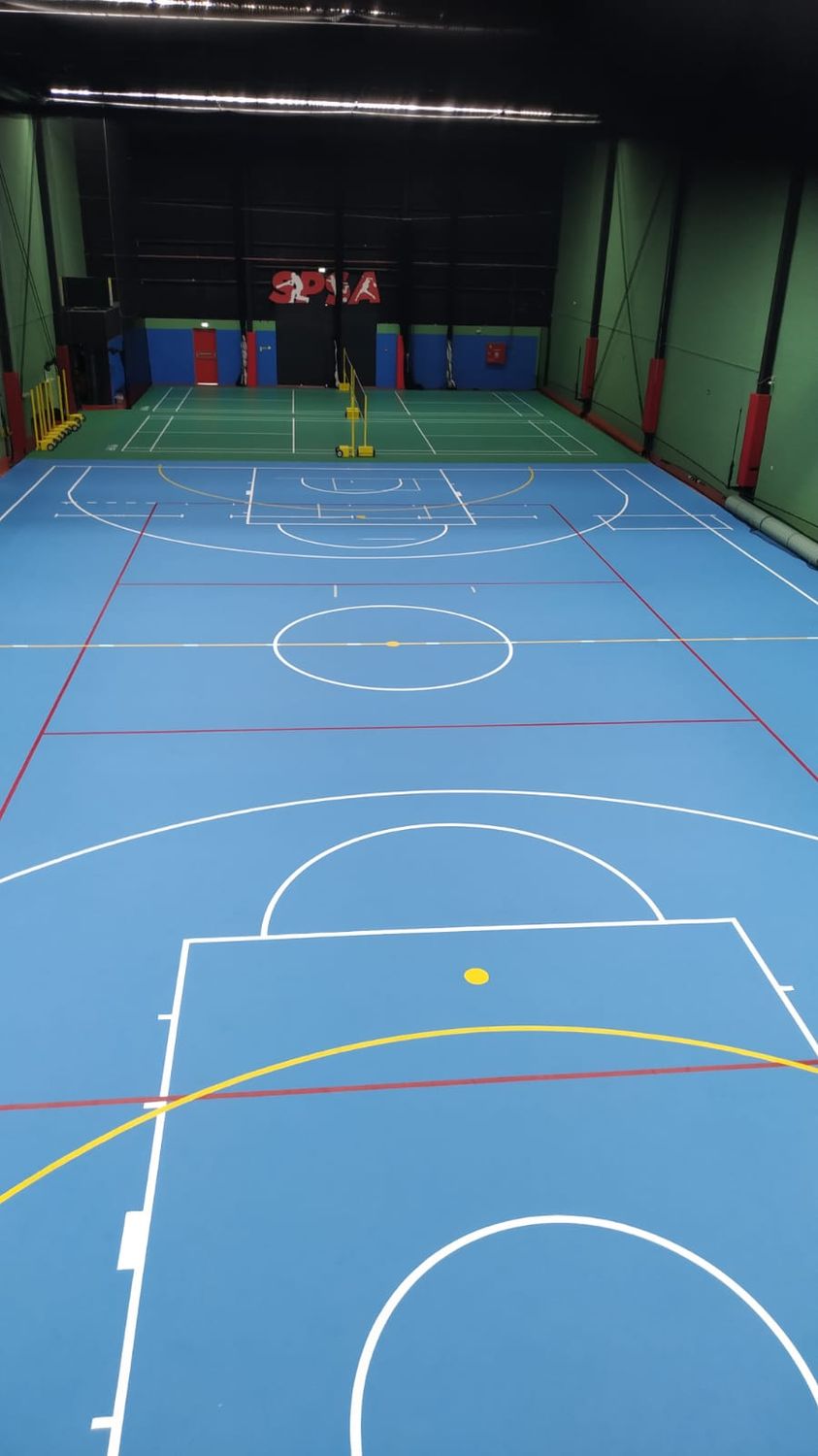 Indoor blue multi-sport court with badminton bay beyond