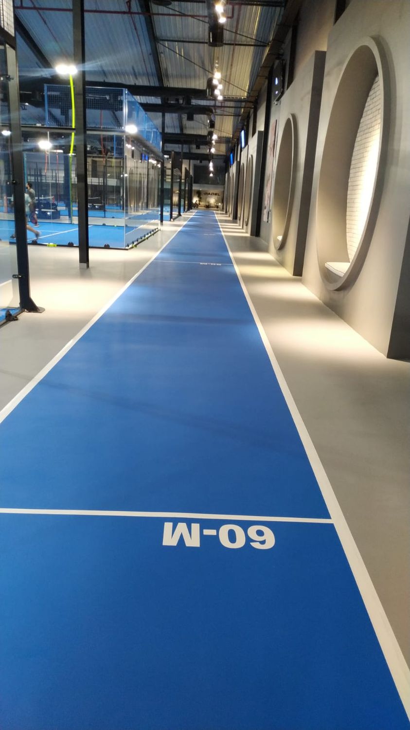 Indoor blue sprint track marked at sixty metres beside padel courts