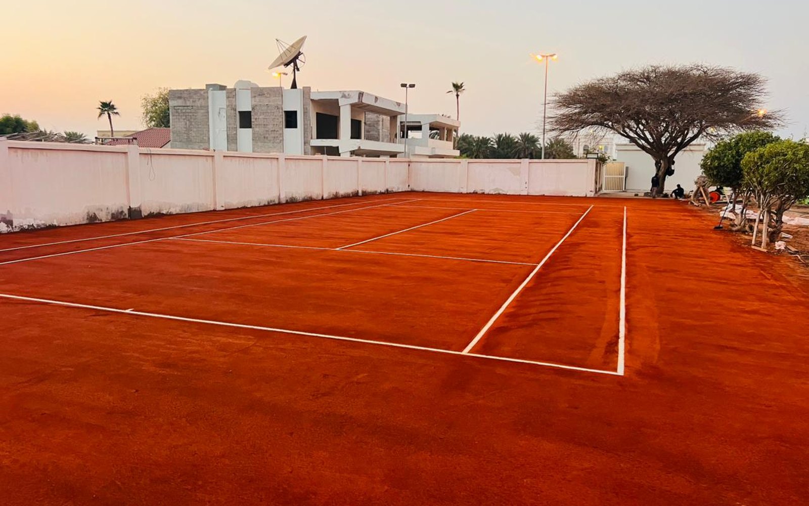 Red clay tennis court with white line markings at dusk