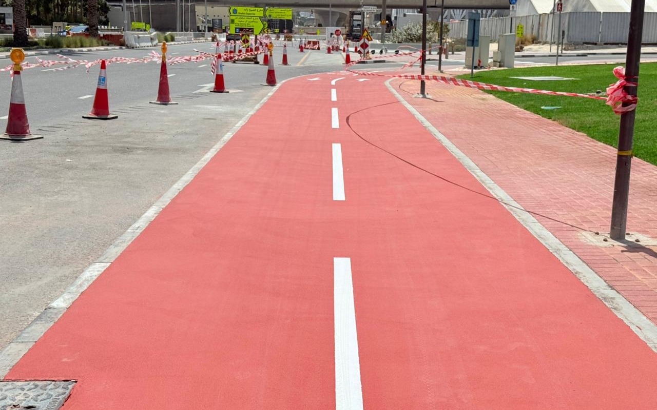 Red acrylic cycle track with white lane markings running alongside a Dubai roadway